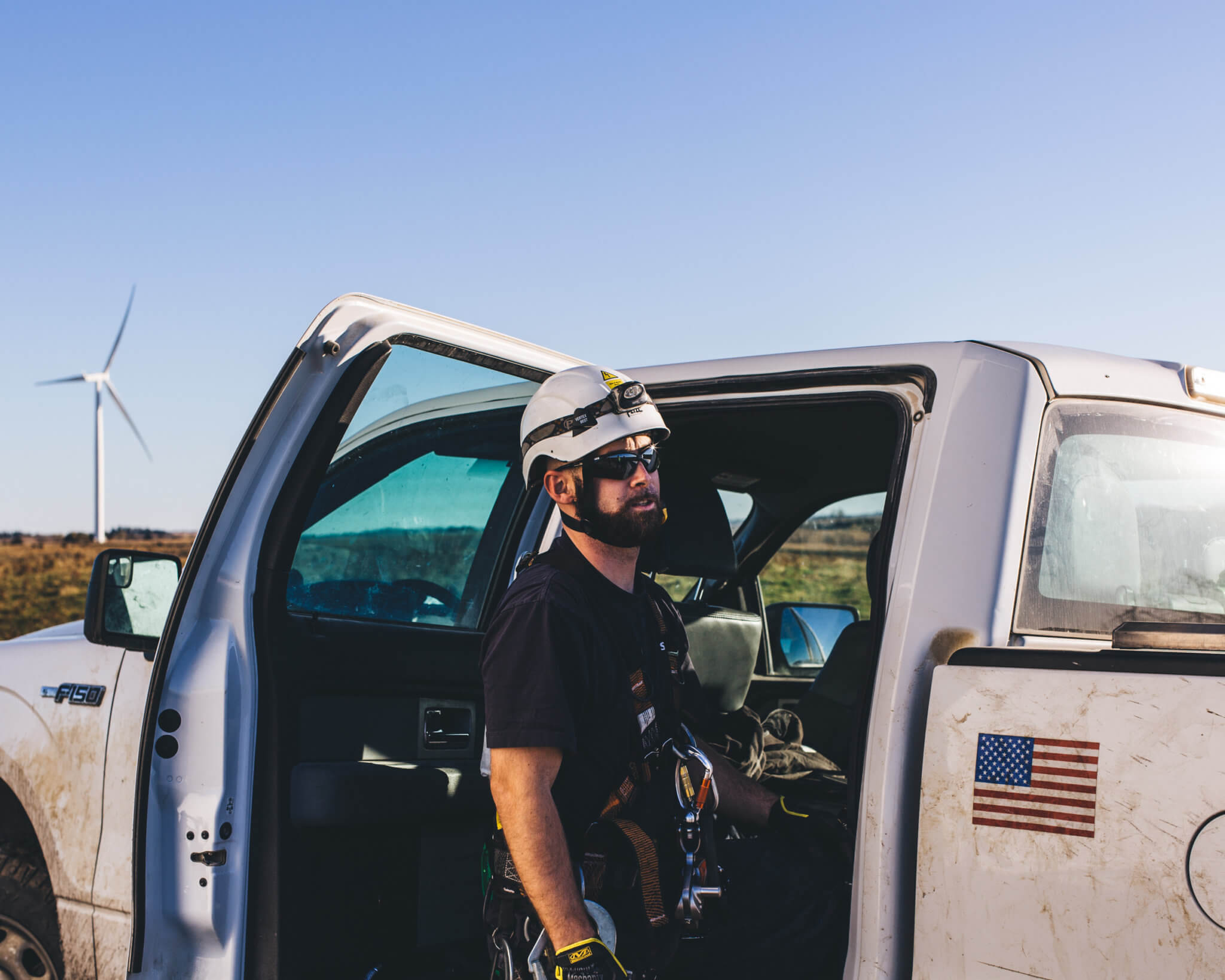 A worker standing in front of a truck with an American flag at a wind power site.