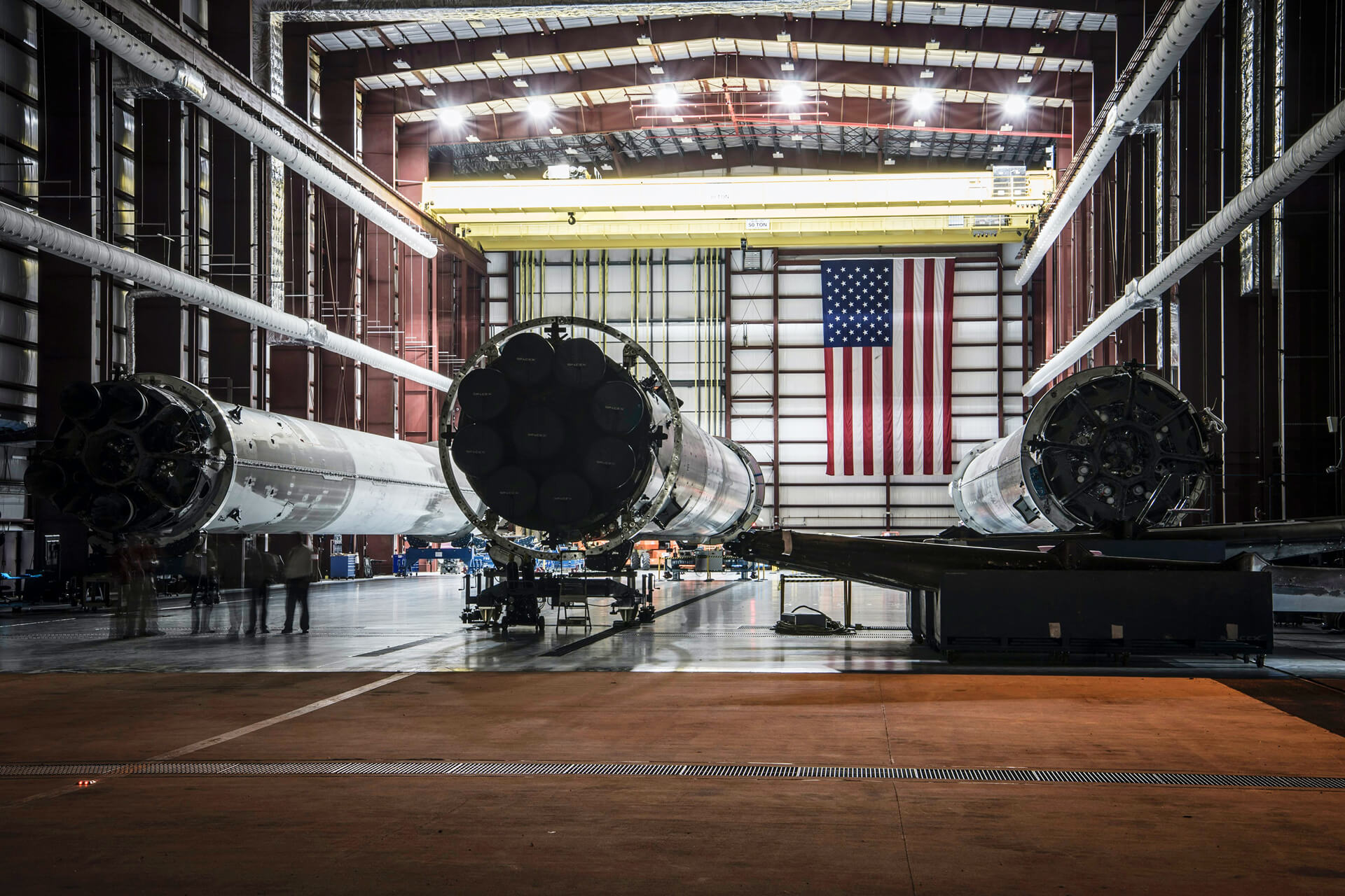 Three SpaceX rockets being prepared at Kennedy Space Center with an American flag in the background.