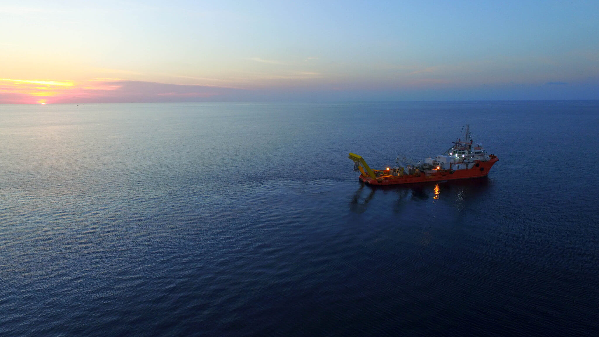 A ship on the ocean at sunrise, laying or inspecting submarine power cables for offshore wind turbines.