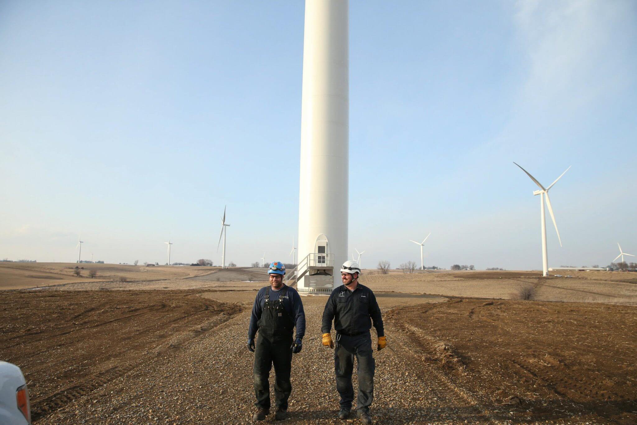Two workers walking towards the camera, away from a wind turbine at a renewable energy project site.