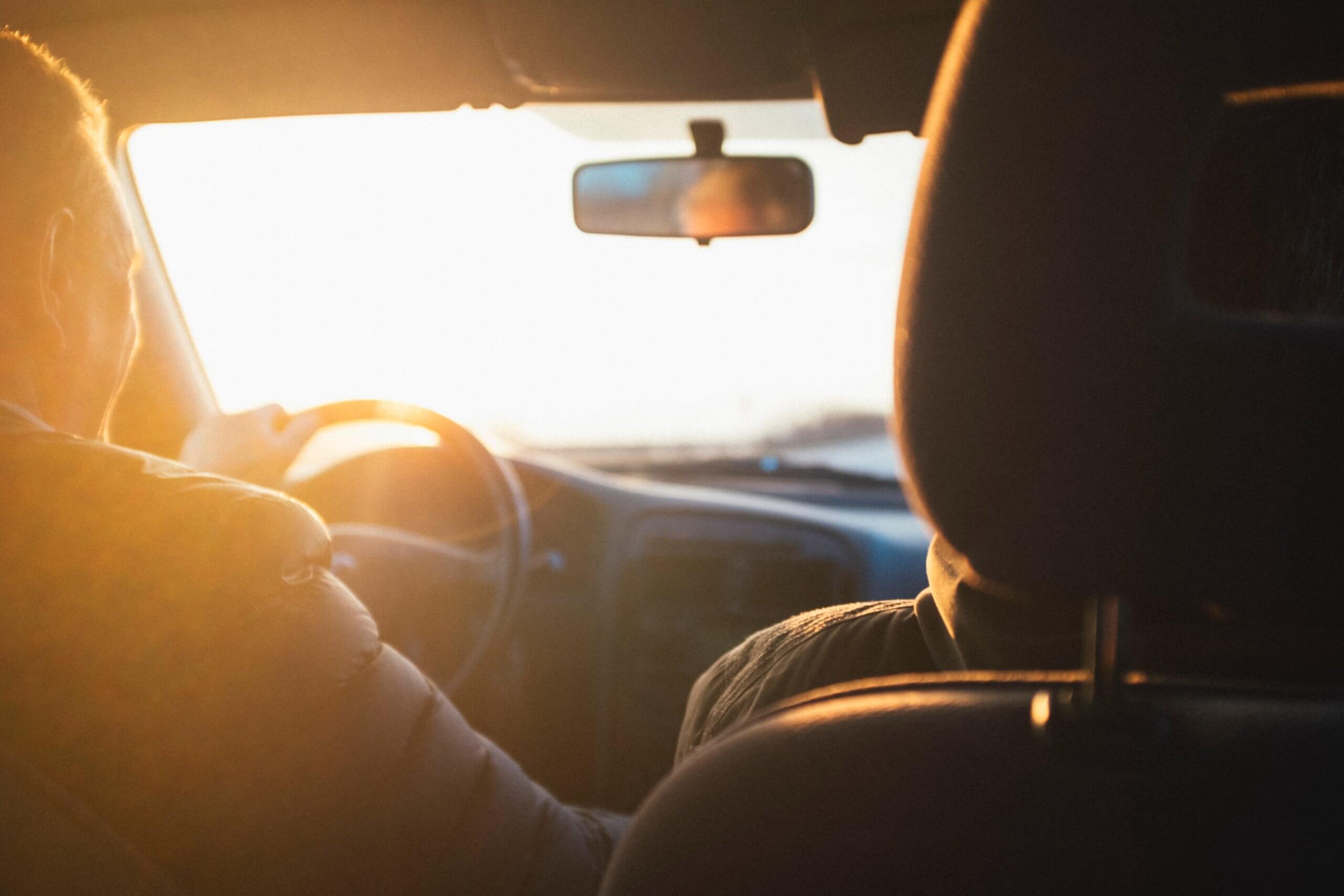 Interior of a car showing a person driving in morning light, taken from the back seat.