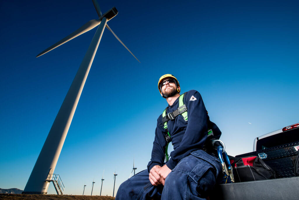 A wind turbine technician in front of an onshore wind turbine farm.