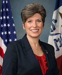 A woman in a blazer in front of two flags
