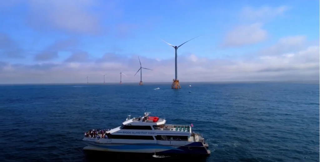 A ferry boat in the ocean with wind turbines behind it