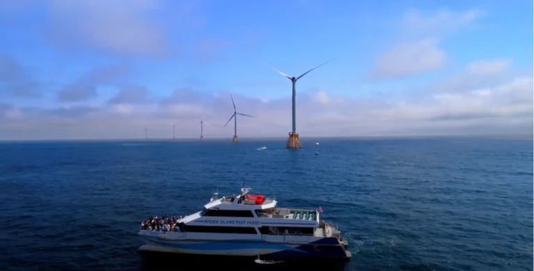 A ferry boat in the ocean with wind turbines behind it