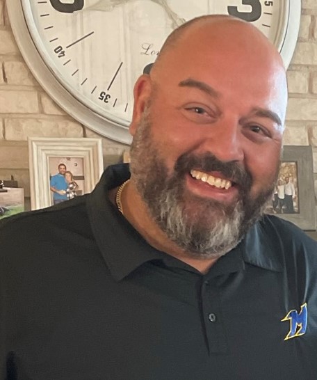 A smiling bald man, with a beard and mustache in a black collared shirt.
