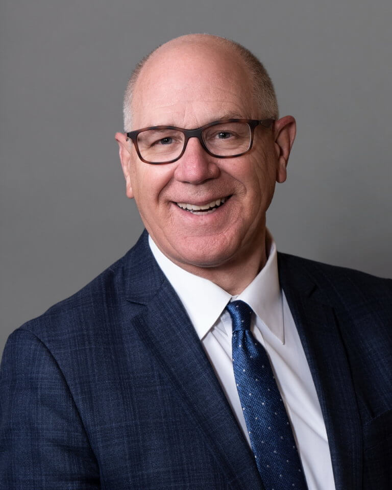A smiling bald man in a blue suit with glasses