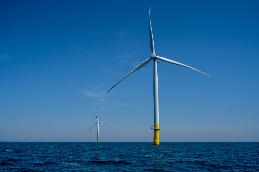 A photo of two wind turbines in a large body of water, one in the foreground, and one in the background.
