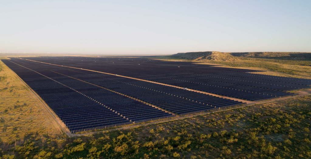 A photo taken from the sky overlooking rows of solar panels that stretch into the distance.