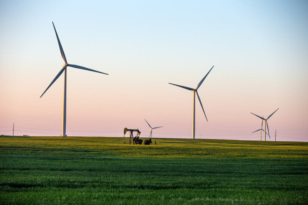 Wind turbines on Kansas prairie with an oil derrick in the foreground.