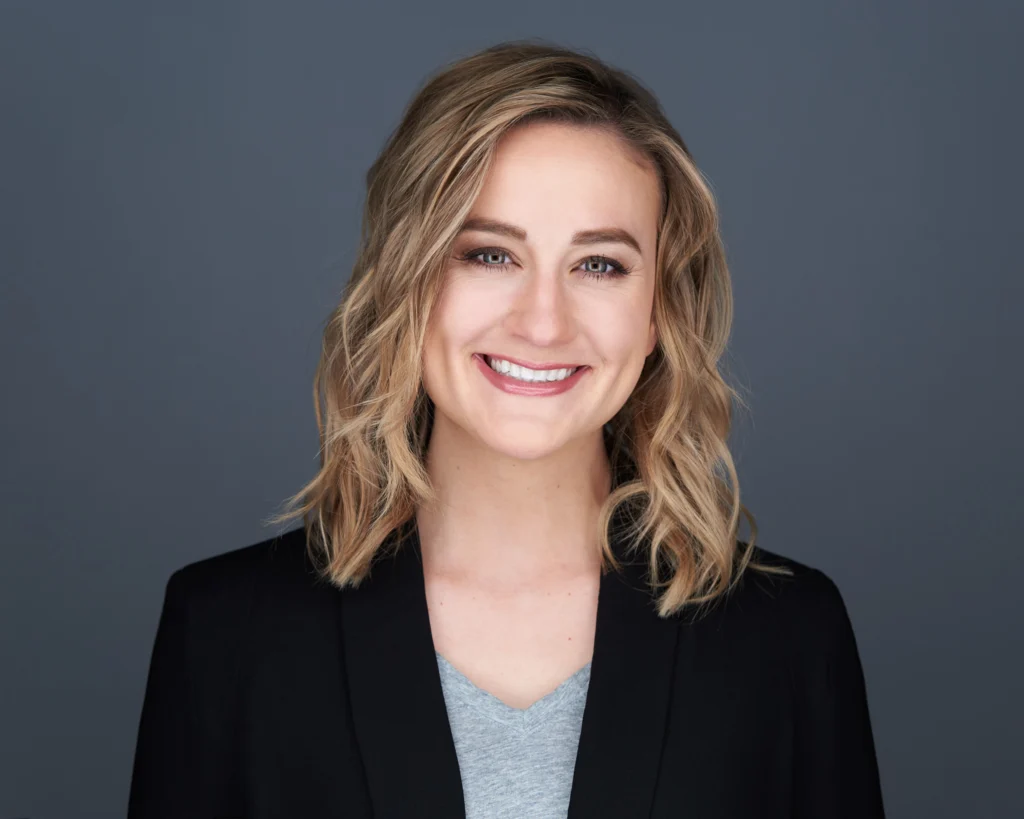 A headshot portrait of Claire Elkin, wearing a black blazer over a grey t shirt.