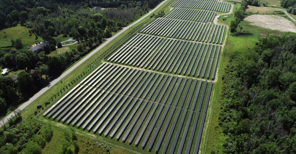 A large solar panel facility nested between a forest and a road.
