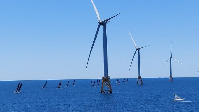 Three offshore wind turbines with sailboats in the background.