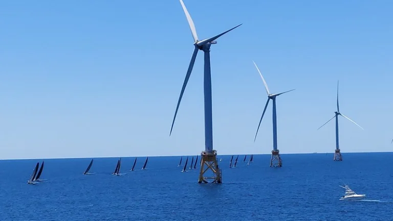 Three offshore wind turbines with sailboats in the background.