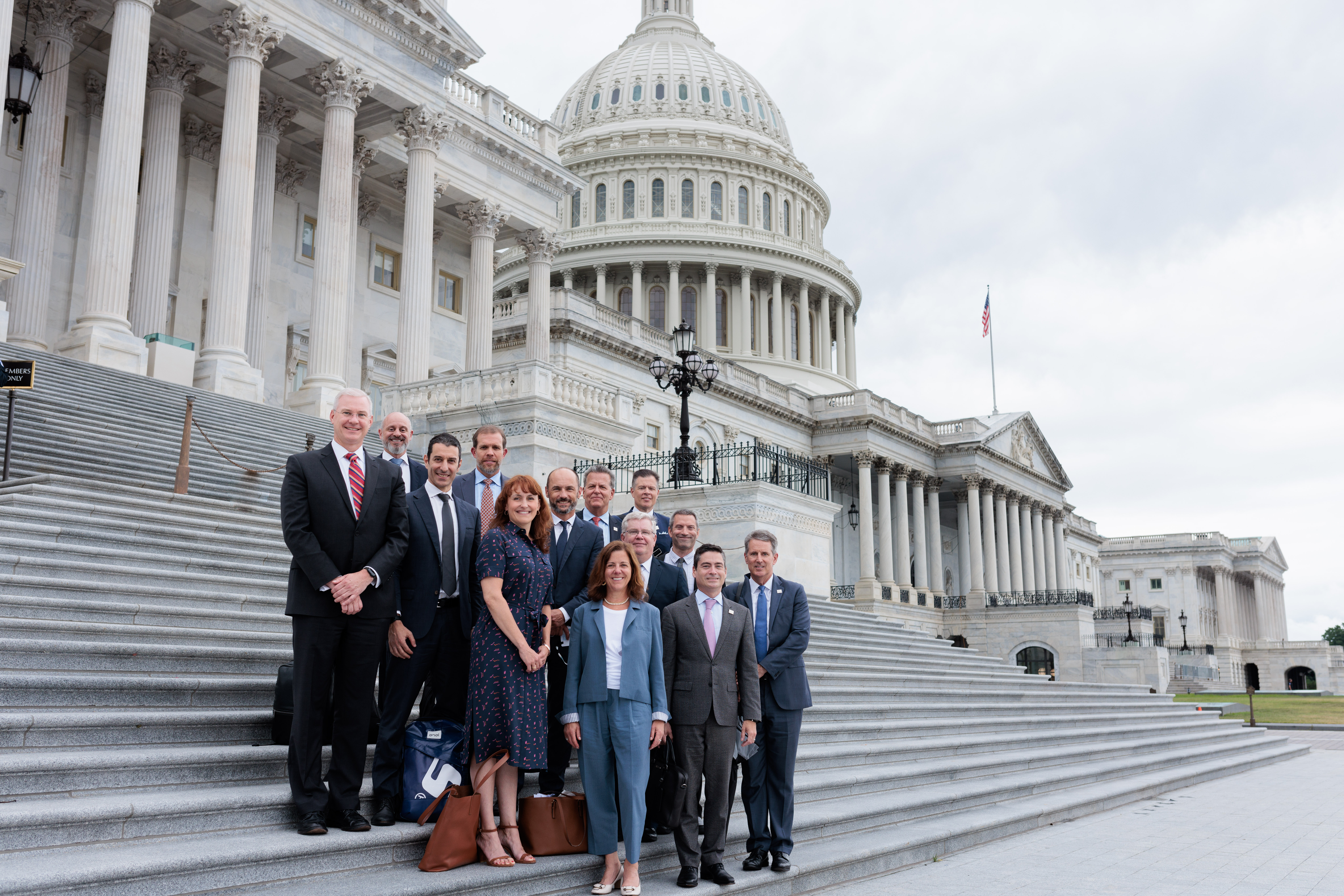 A group of people in formal dress pose for a picture on the Capitol steps.