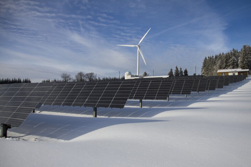 Solar panels and a wind turbine with snow on the ground.