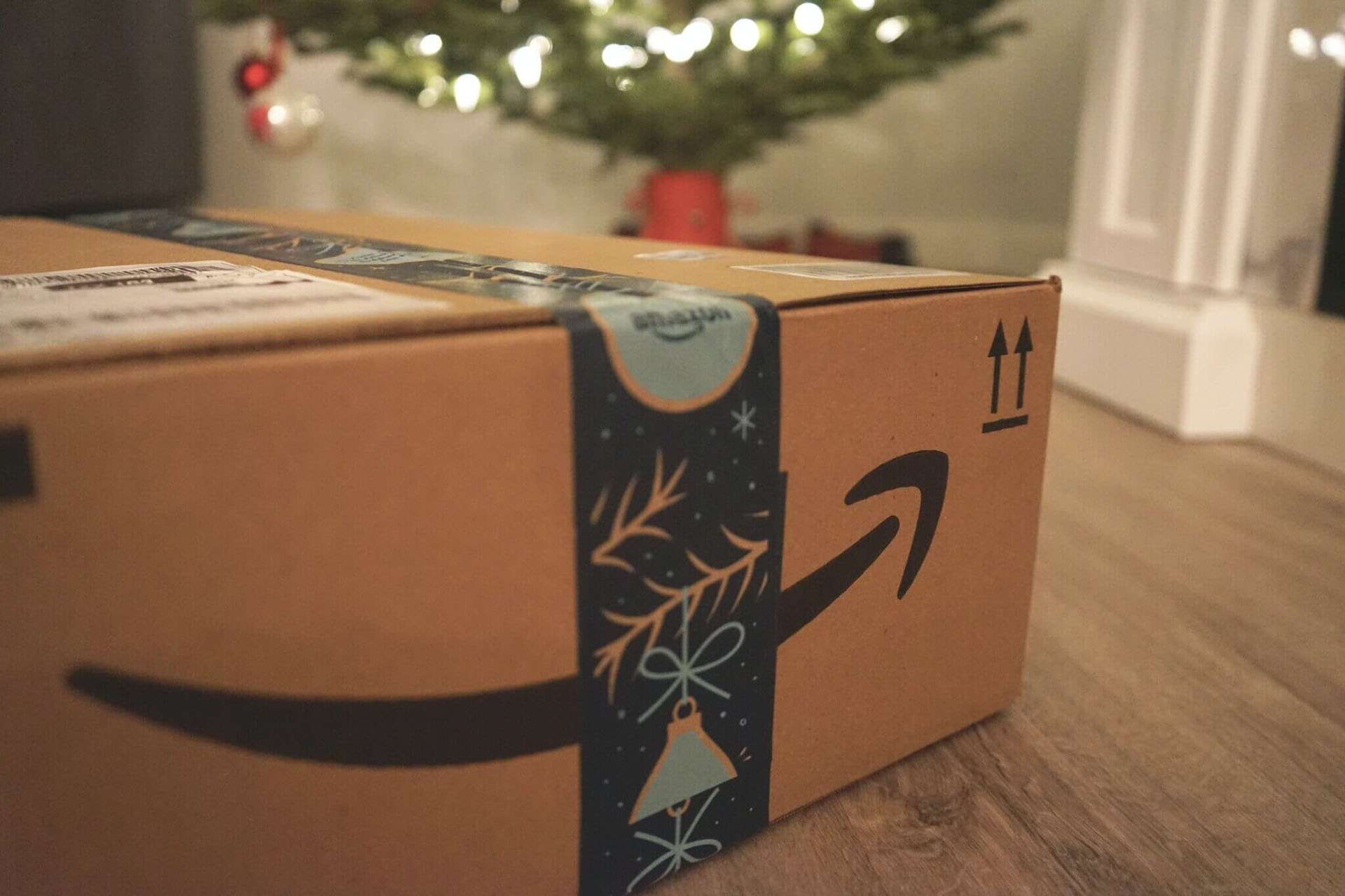 A close-up photo of an Amazon delivery box on the floor with a Christmas tree visible in the background.