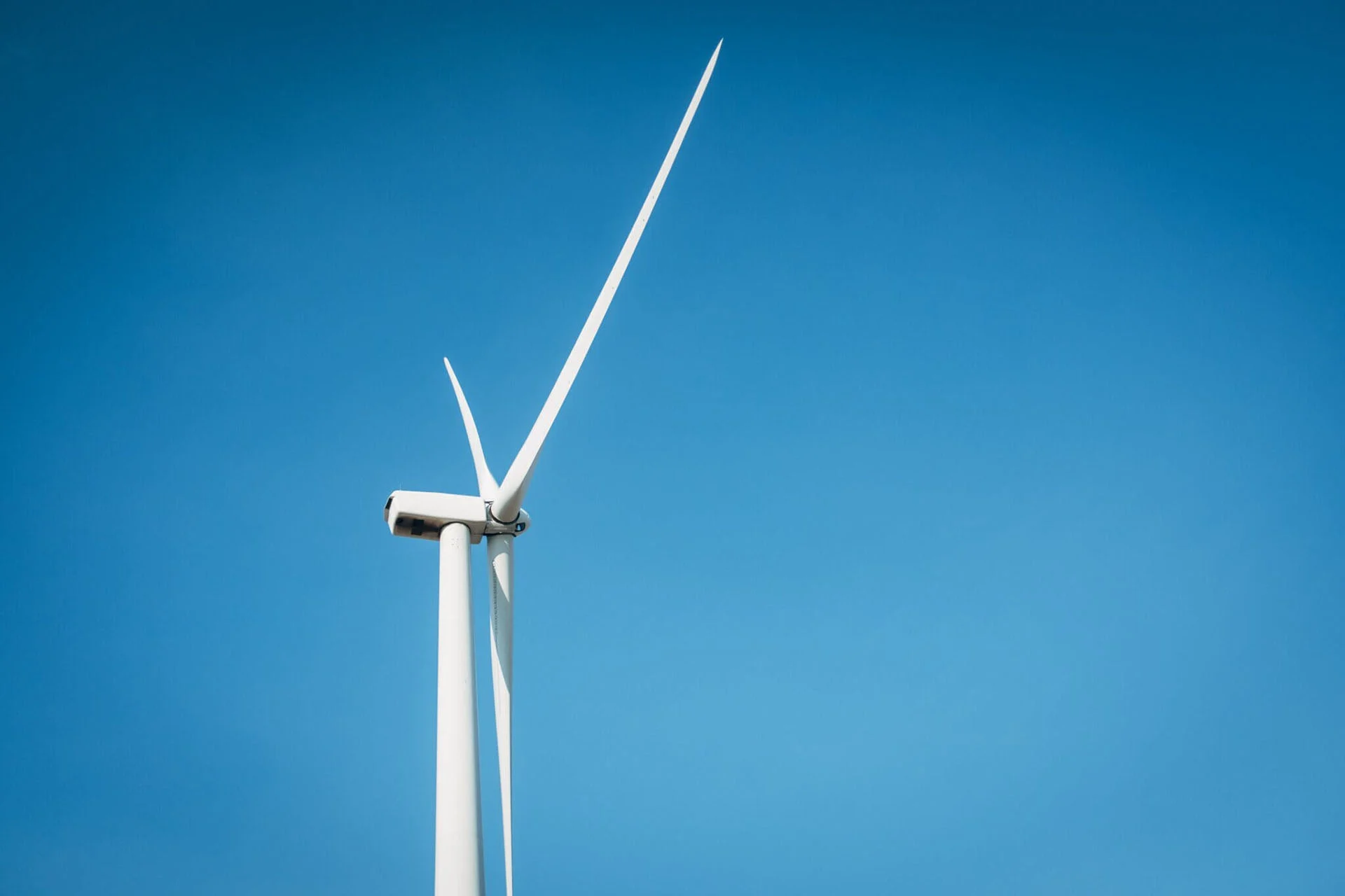 A photo of a single wind turbine against a clear blue sky.