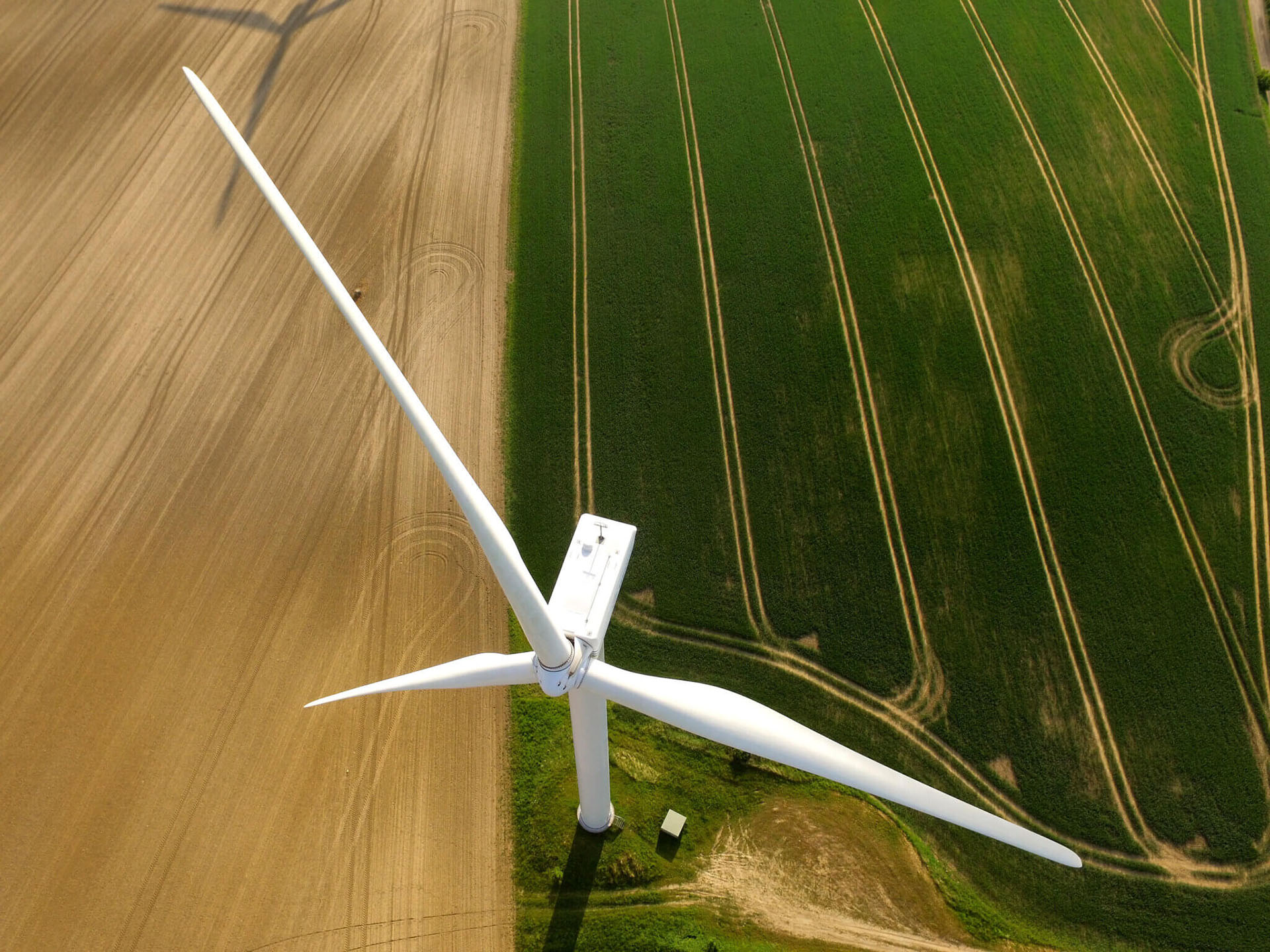 An aerial photo of a single wind turbine in the middle of green farmland.