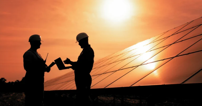Two Energy Technicians Look Over Plans in Front of Photovoltaics at Sun Down.