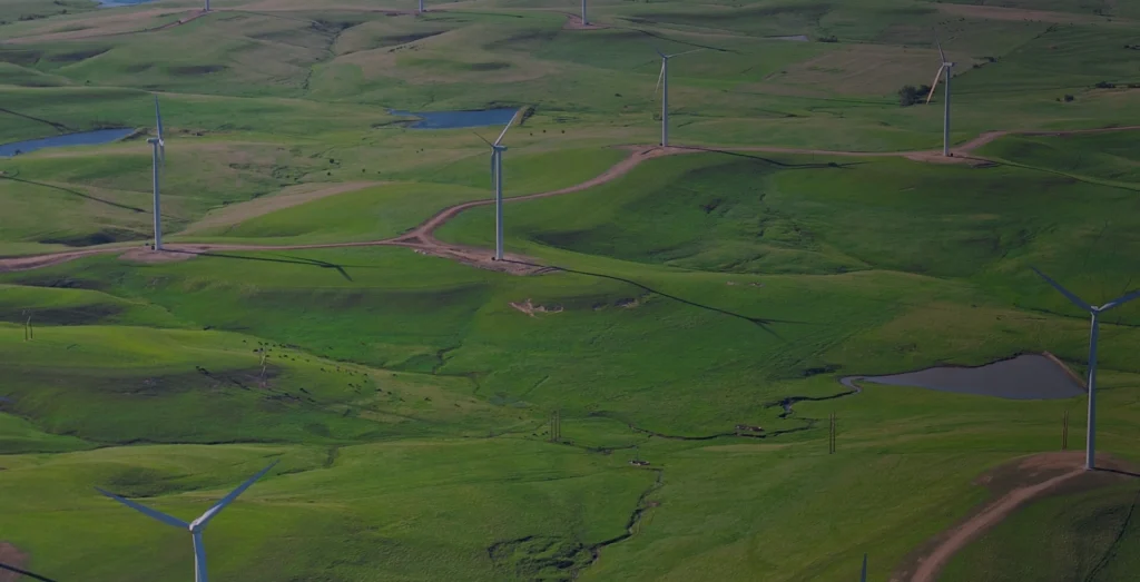 A wind turbine stands tall in a landscape of rolling green hills.