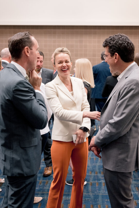 Two attendees at an ACP conference networking and laughing with ACP CEO Jason Grumet.