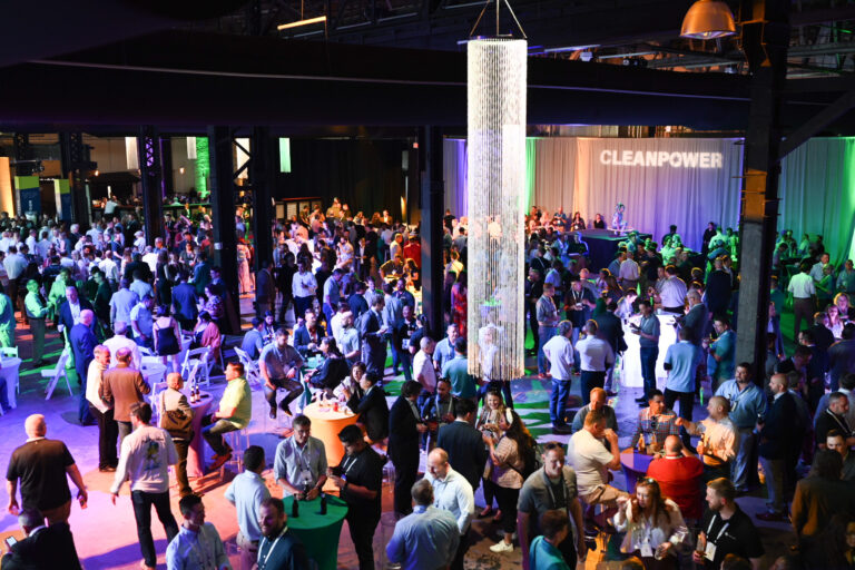 An aerial view of ACP's CLEANPOWER Conference attendees in New Orleans participating in the event's opening reception. A room full of people fraternizing with purple and green lights and the CLEANPOWER logo.