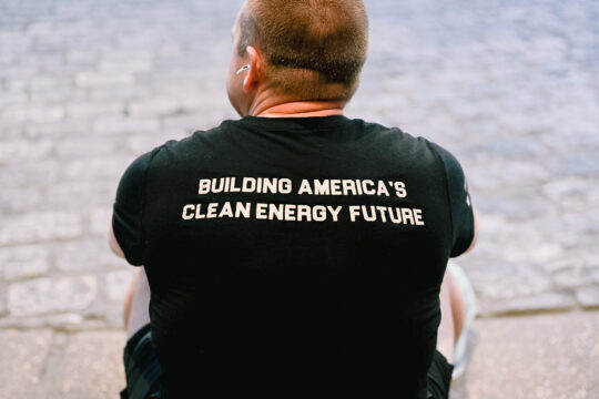 A man sitting down in a t-shirt that says "Building America's Clean Energy Future" across the back.
