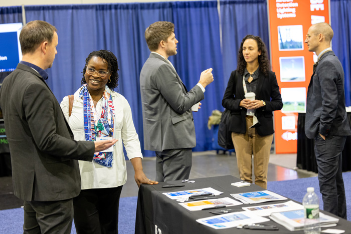 Five conference attendees at an American Clean Power (ACP) event networking and chatting on the exhibit hall floor.