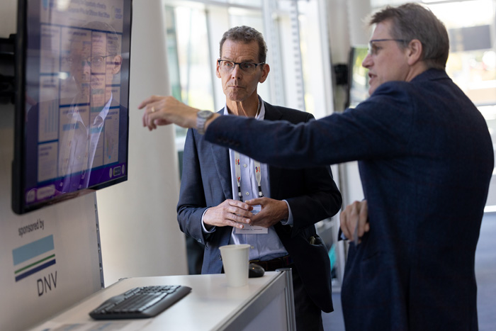Two attendees at an ACP conference, one of which is demonstrating to the other by pointing at a digital screen.