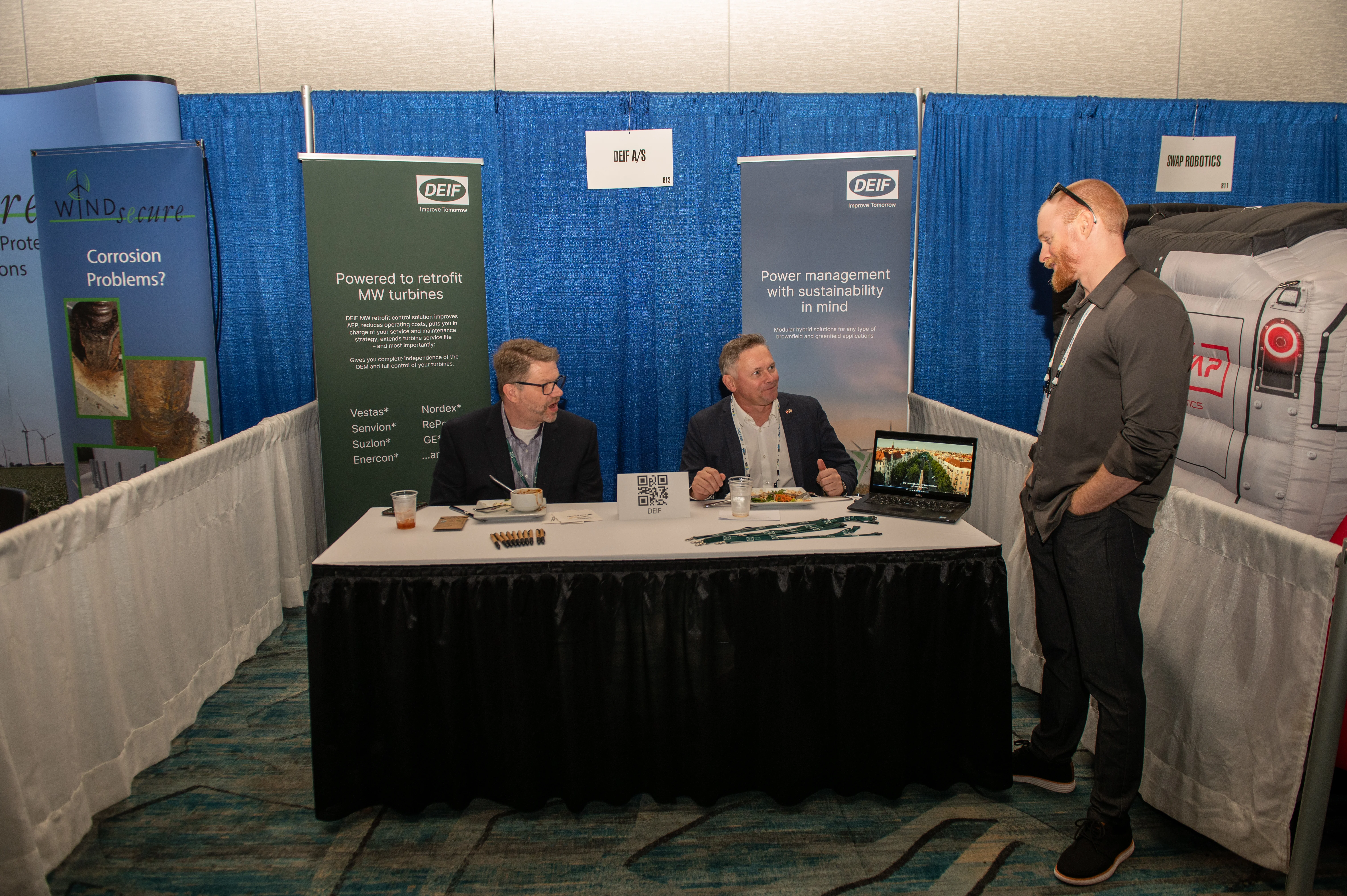Two ACP Offshore Windpower exhibitioners eating lunch and chatting with a conference attendee.