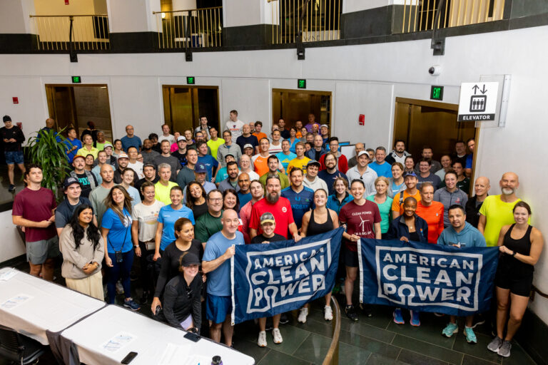 Participants in ACP's Offshore WINDPOWER Conference 2023 5k Fun Run gathered in a lobby holding American Clean Power flags.