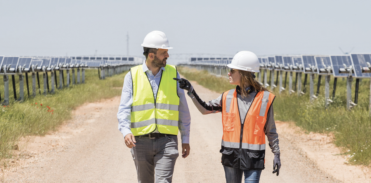 Two workers in hard hats walking through a field of solar panels in deep conversation.