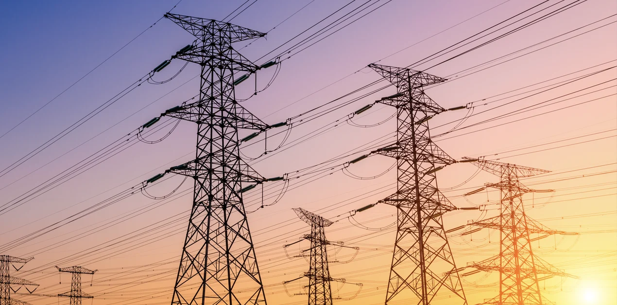Several transmission lines and towers silhouetted against a multi-colored sky.