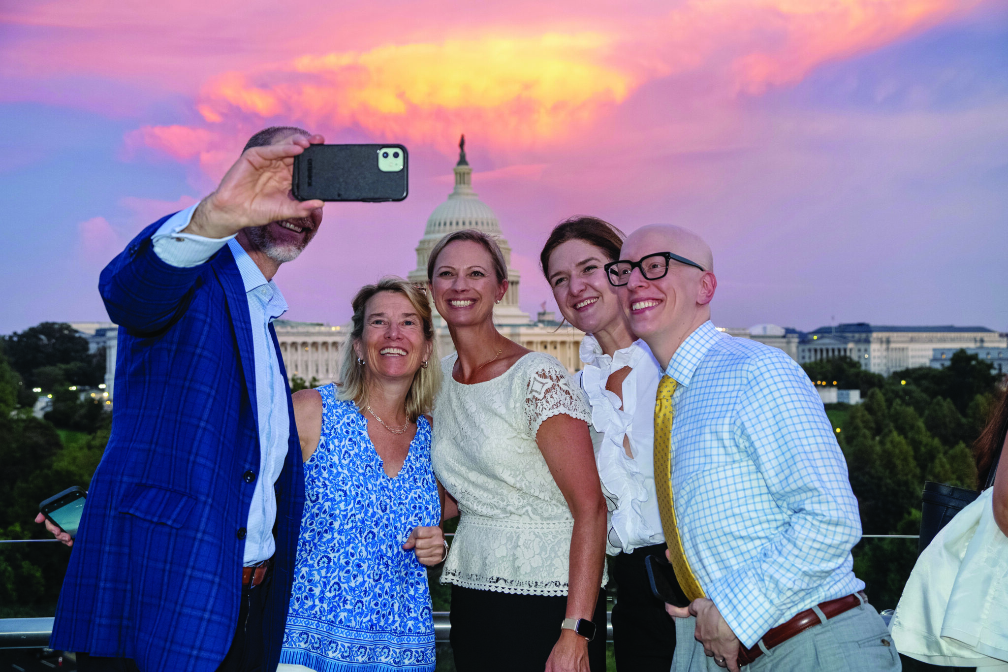 People smiling, taking a selfie at sunset with the U.S. Capitol in the background.