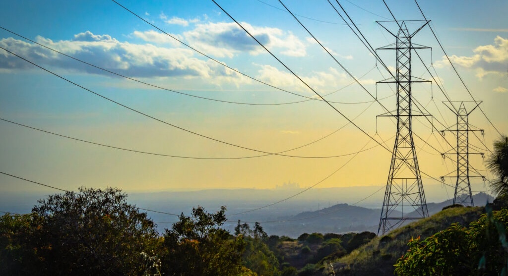 two transmission towers seen looming over greenery with a city visible in the distance